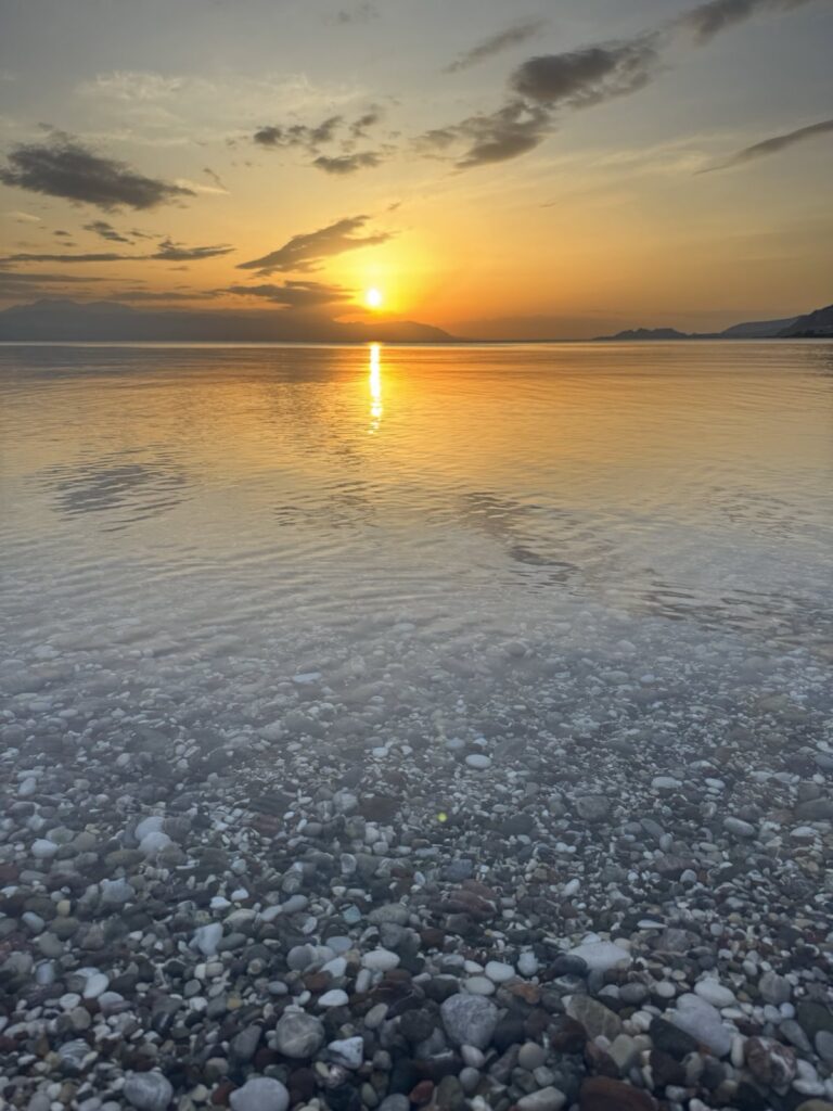 Solnedgång vid Loutraki med stilla vatten och stenar.