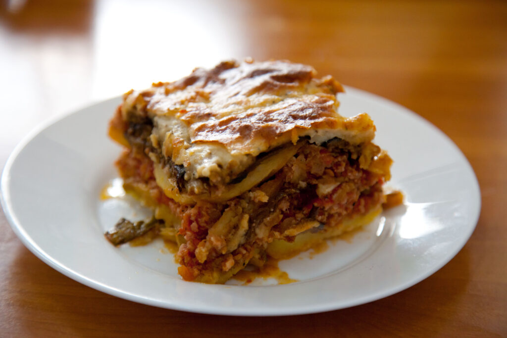 En bit grekisk moussaka med aubergine, köttfärs och béchamel på en vit tallrik